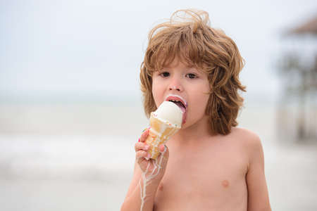 Outdoor closeup portrait of cute kid eating ice cream in summer hot weather.の写真素材