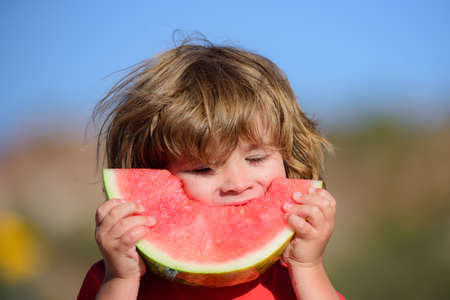Close-up portrait of happy little child eating sweet watermelon.の写真素材