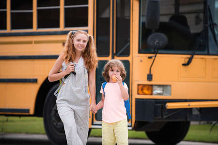 Elementary school students on school bus. Little ready to study. Happy little brother and sister standing together in front of school bus.の写真素材