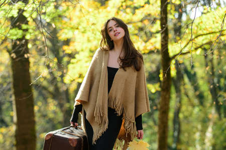 Autumn girl with suitcase walking on leaves and fall yellow maple background. Beautiful woman in...
