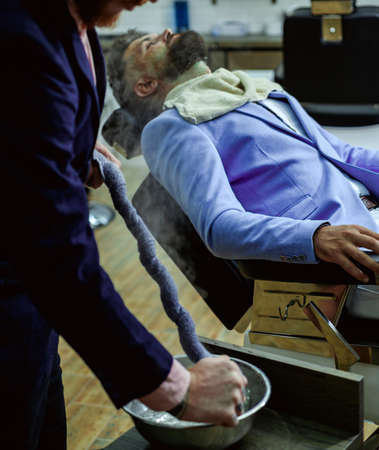Making haircut look perfect in barbershop. Barber shaving bearded man in barbershop. Hairdresser...