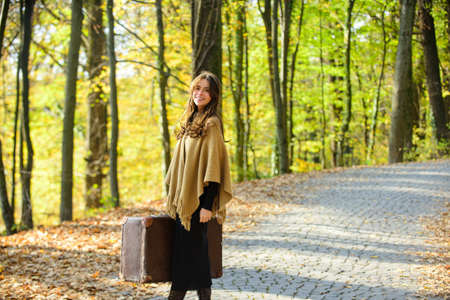Autumn Woman traveler. Hipster girl hold retro old suitcases on autumn leaves background. Beautiful woman in autumn park.の写真素材