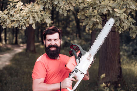 Firewood as a renewable energy source. Woodcutter with chainsaw on sawmill. Harvest of timber. Man doing mans job. Lumberjack on serious face carries chainsaw.の写真素材