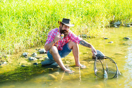 Happy bearded fisherman with tattoo. Fly fishing adventures. Man relaxing nature background. Activity and hobby. Successful catch. Man fishing on river. Man catching fish. Perfect weekend.の写真素材