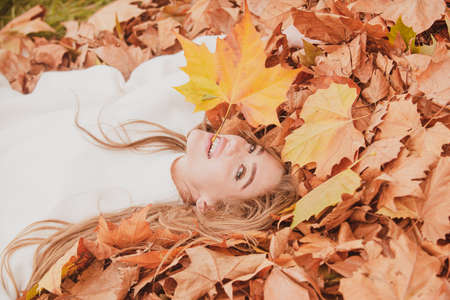 Autumn happy, smiling girl lies in maple, yellow leaves.の写真素材