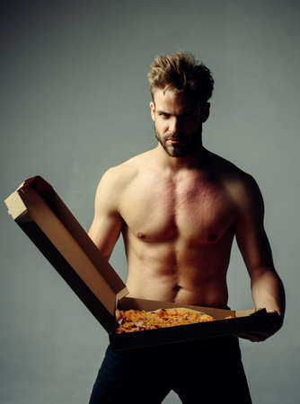 Strong brutal bearded man holding an italian tasty pizza isolated at gray background.   pizza deliver with   muscular torso. Handsome hungry man with food fetish.の写真素材