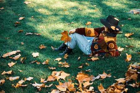 Large maple leaf in a female hand. Woman holding fall maple leaves. Autumn girl in city park. Fallen...