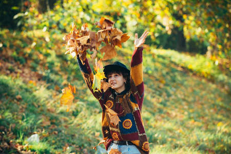 Beautiful young woman throwing leaves in a park. Happy girl playing with autumn leaves in the park....