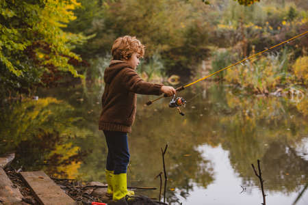 Kid with fishing-rod. Child fishing at autumn lake.の写真素材