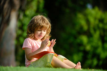 Distance children education. Cute little boy studying and eating apple outside in park.の写真素材
