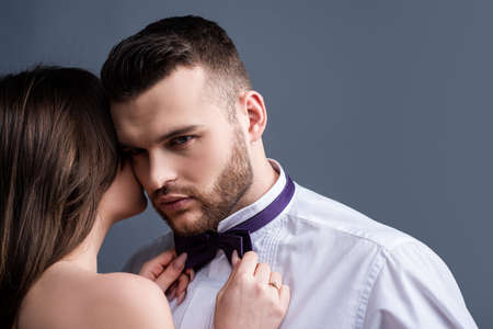 Woman holds mans bowtie, bow tie. Sexy couple in love. Sensual lovers undressed. Girlfriend and...