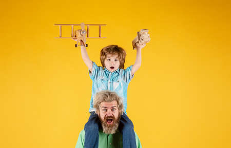 Father and son together. Boy child is sitting on daddy shoulder piggyback while the flight. Kid boy pilot.の写真素材