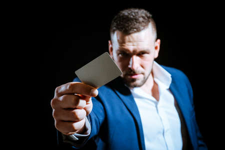 Young man giving his credit card looking at the camera, black background. Business man paying with a...
