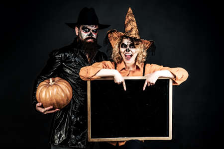 Halloween couple in witch hat and costume holding blackboard, blank copy space, empty banner,...