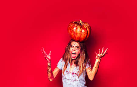 Funny halloween portrait of crazy woman on red background isolated. Bloody girl with pumpkin.の写真素材