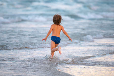 Happy child running in the sea. Kid boy having fun on the beach. Summer vacation and healthy kids.の写真素材