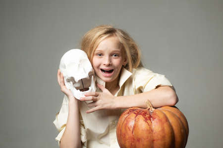 Blond woman in costume witch and hold halloween pumpkin. Happy laughing child girl in witch costume to halloween. Cheerful little witch hold skull. Halloween party. Halloween celebration.の写真素材