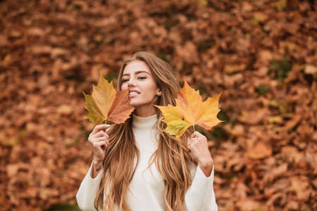 Happy smiling woman holding in her hands yellow maple leaves over autumn background.