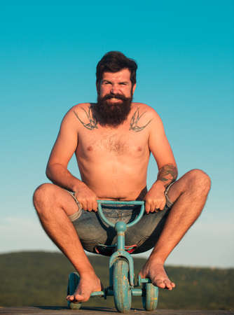 Guy riding childs tricycle. Funny man on a bicycle. Emotional crazy guy on a childrens bike.の写真素材