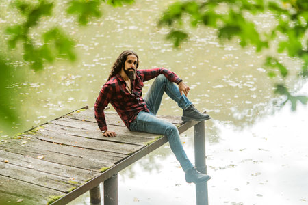 Young man in countryside. Handsome guy relax on lake, nature outside.