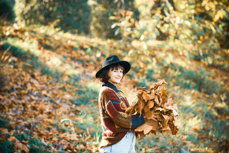 Girl holding yellow autumn leave. Autumn walk. Beautiful elegant woman standing in a park. Happy girl playing with autumn leaves in the park.の写真素材