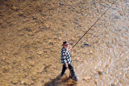 Mature man fishing on the pond. Happy fly fishing. Angler catching the fish. Master baiter. Catching...