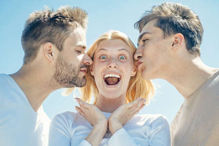 Blonde happy girl getting kisses from two handsome boys. Charming woman standing between two...