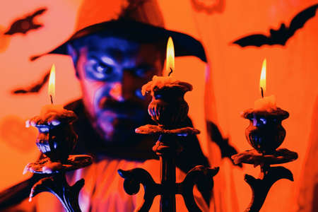 Evil witcher with red hair and a beard in a black cloak reading a book of spells. Mystery and horror concept. Wizard, sorcerer, warlock. Jack o lantern.の写真素材