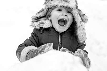 Excited Child playing with snow in park on white snow background. Winter children in frosty winter Park. Cute kid - winter portrait. Snowman and funny little boy kid in the snow.の写真素材