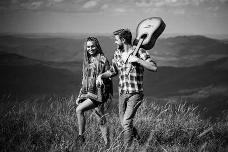 Sweet harmony in mountains. Happy couple of travelers have a walk, smile and play guitar.の写真素材