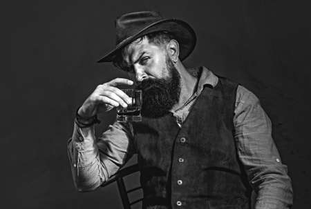 Stylish elegant bearded man Bartender holds whiskey glass. Luxury beverage concept. Fashionable man in white shirt and suspenders.の写真素材
