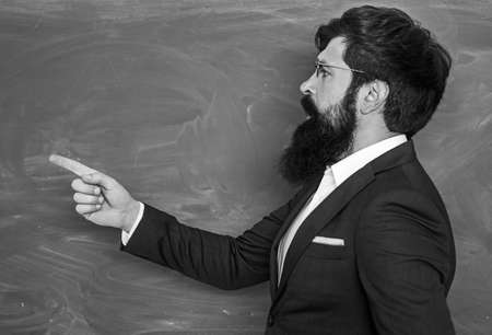 Bearded professor at school lesson at desks in classroom. Education. Chalkboard copy space. Friendly teacher in classroom near blackboard desk.の写真素材
