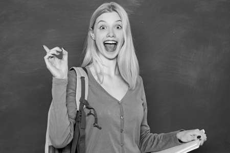 Happy girl holding book and looking at camera while standing in classroom. Student with backpack. Looking for volunteers. High school education. Formal education. Improving myself through educationの写真素材