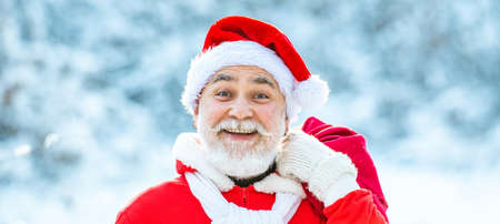 Delivery christmas gifts. Winter Christmas greeting card. Santa Claus with big bag. Santa Claus with bag walking in winter.の写真素材