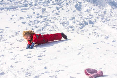 Child laying down in the snow on winter day. Funny Christmas. Kid on walk in nature. Kids play and...