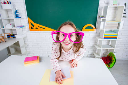 Funny schoolgirl preschool with fun glasses in school near blackboard.の写真素材