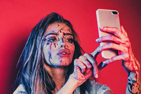 Makes selfie. Halloween make up. Halloween bloody woman on red background isolated.の写真素材
