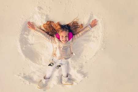Snow angel made by a kid in the snow. Smiling child lying on snow with copy space. Funny kid making snow angel.の写真素材