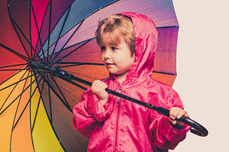 Cute little boy are preparing for autumn rain day. Cheerful boy in raincoat with colorful umbrella....