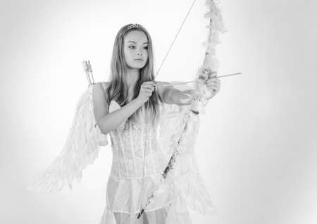 Concept of innocent girl. Angel in love. Valentines day card. Cupid girl aiming at someone with an arrow of love. Happy teenage angel girl.の写真素材