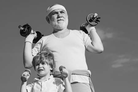 Body care and healthcare, old vs voung. Grandfather and child lifting weights. Senior man and child in family health club. Father and children having workout.の写真素材