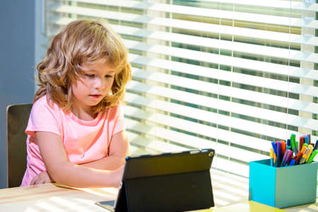 Smart and attractive boy using tablet on desk at home. Online education concept. Kids education,...