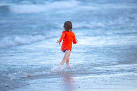Blonde boy running and having fun on the beach on blue sea in summer.の写真素材