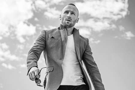 Man with confident face and brutal style. Advertising for clothing store. Standing on the pure blue sky background next to copyspace. Fashionable man in leather jacket.の写真素材