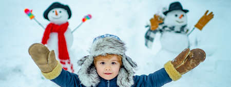 Child playing with snow in park on white snow background. Happy child playing with snowball against...