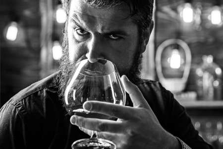 Man with beard in black with glass of beverage. Bearded man holds glass of brandy. Bearded hipster drink cognac. Stylish rich man with glass of scotch. Drinks brandy or whiskey. Tasting.の写真素材
