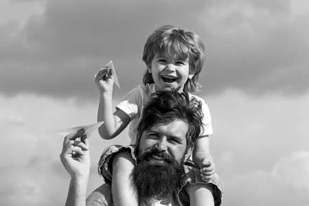Generation. Father giving son ride on back in park. Father and son building together a paper airplane. Portrait of happy father giving son piggyback ride on his shoulders and looking up.の写真素材