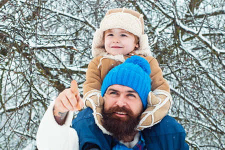 Father giving son ride on back in park. Child sits on the shoulders of his father. Portrait of happy...