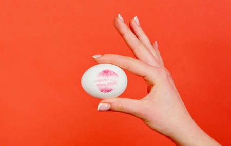 Print of red lips on white egg. Red lip imprint on easter egg on red background.