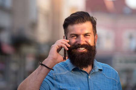 Happy hipster modern business man with beard walking in town and calling on mobile phone.の写真素材